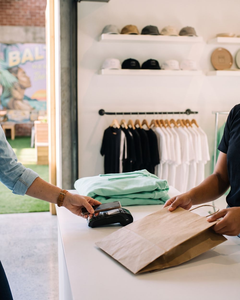 Sarah taps her phone on the card reader as Jess passes her the shopping bag