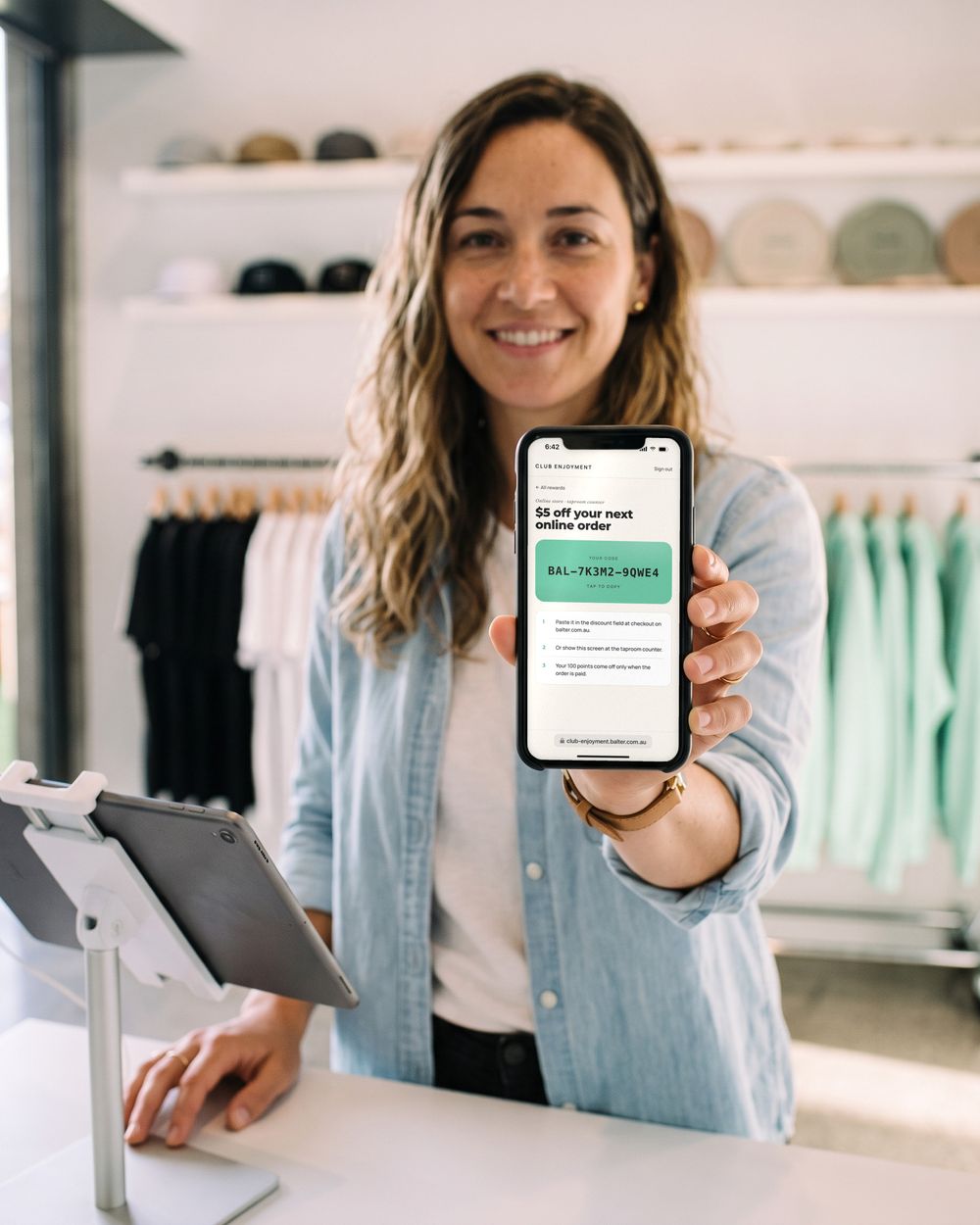 Sarah shows her $5-off reward code on her phone across the merch shop counter