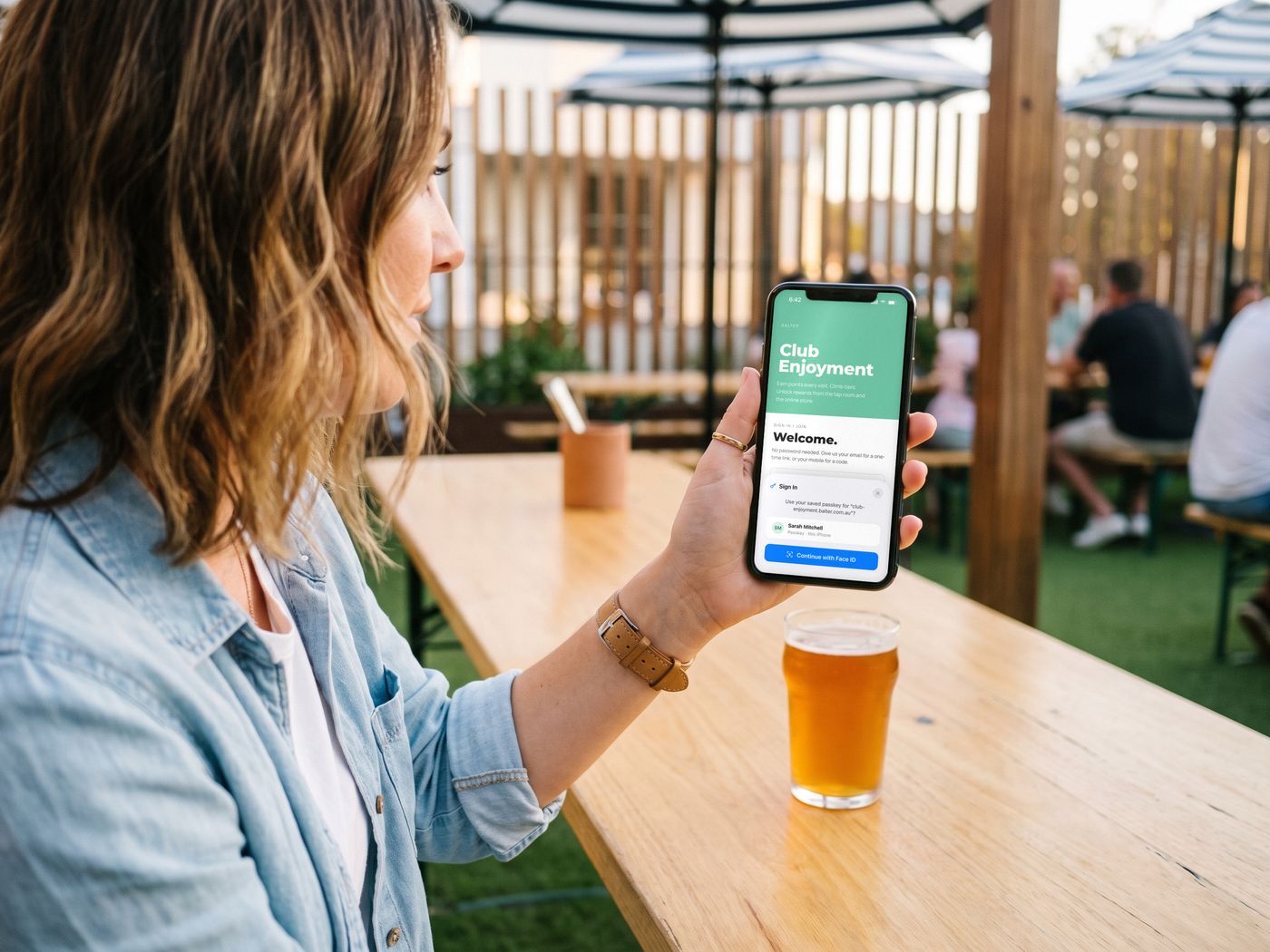 Under the striped umbrellas in the beer garden, Sarah signs in to Club Enjoyment with a passkey and Face ID